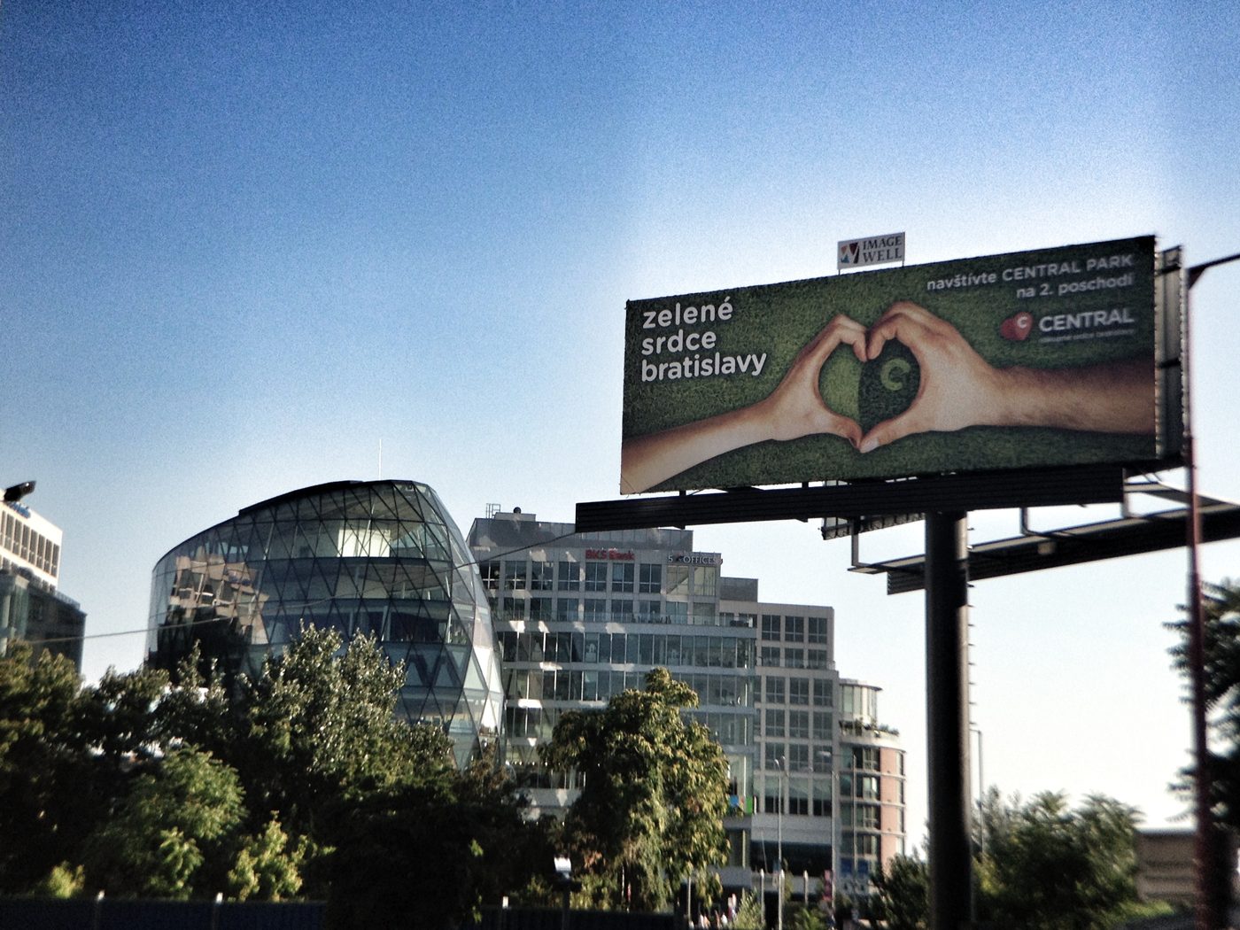 Billboard „Zelené srdce Bratislavy" pred nákupným centrom Central, v pozadí sklenená budova