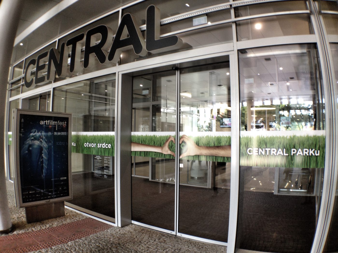 Polep sklenených dverí vchodu do centra: pás trávy, ruky zložené do srdca a text otvor srdce Central Parku